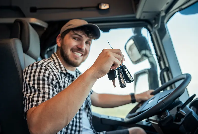 Smiling driver holding keys inside truck.